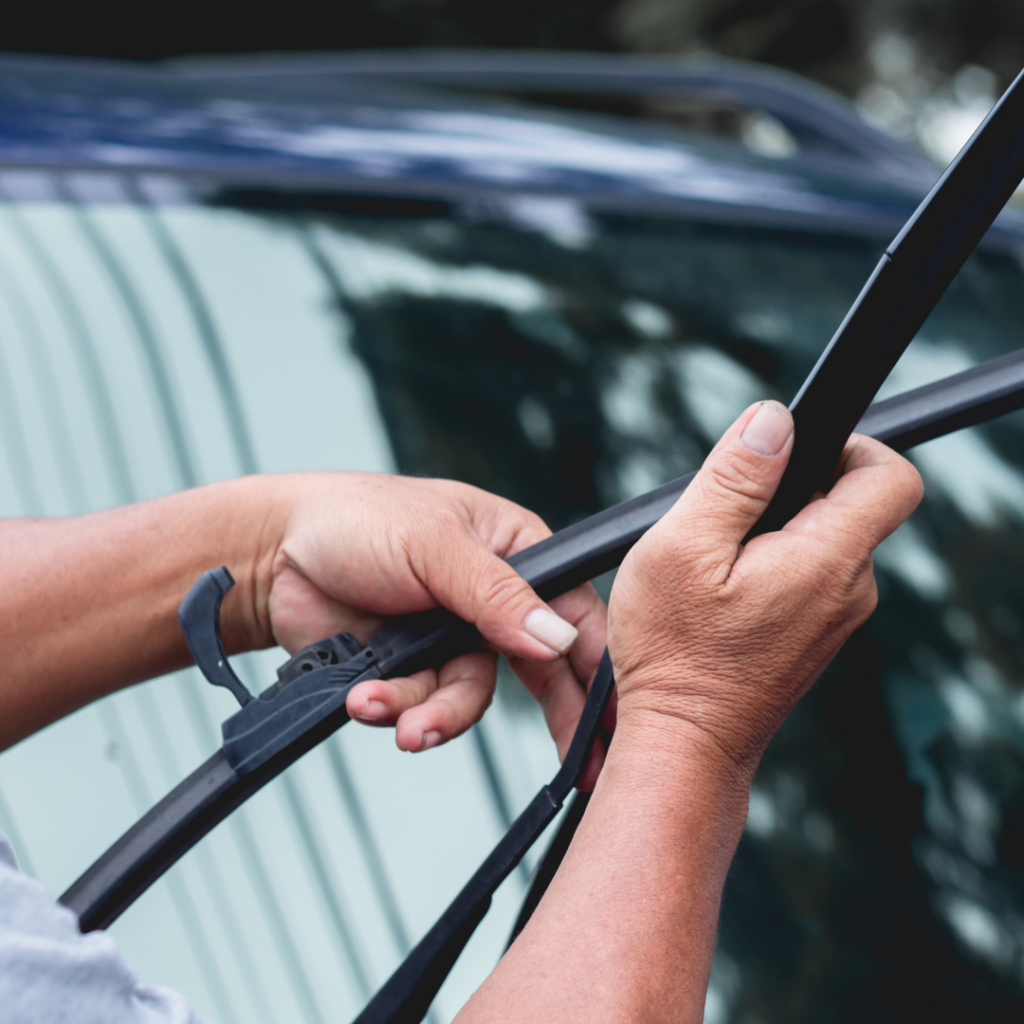 due mani che stanno sostituendo la spazzola del tergicristalli di un'auto